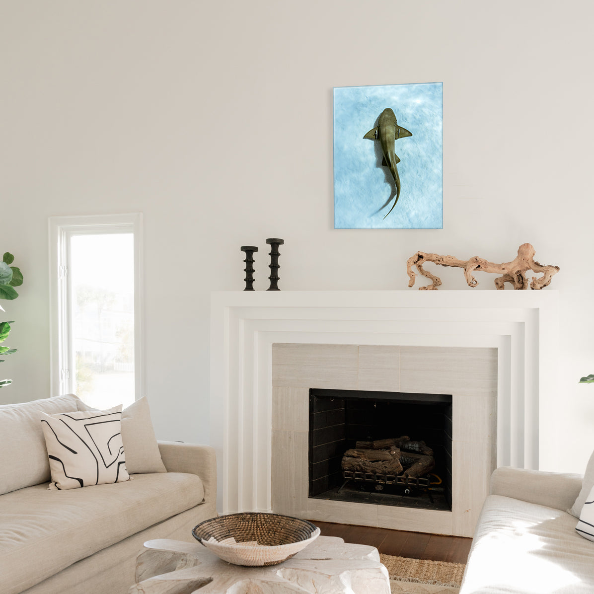Living room with a fireplace and a glass print of a shark swimming above sand on the wall