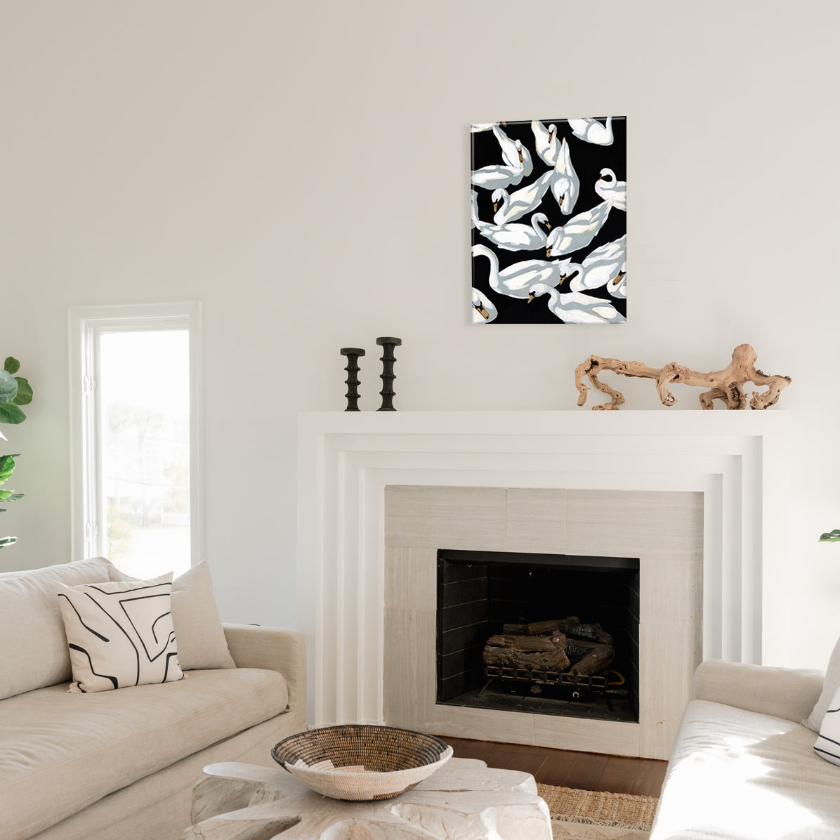 Living room with a fireplace, couch, and glass print of swans painted on a black background above the mantel.