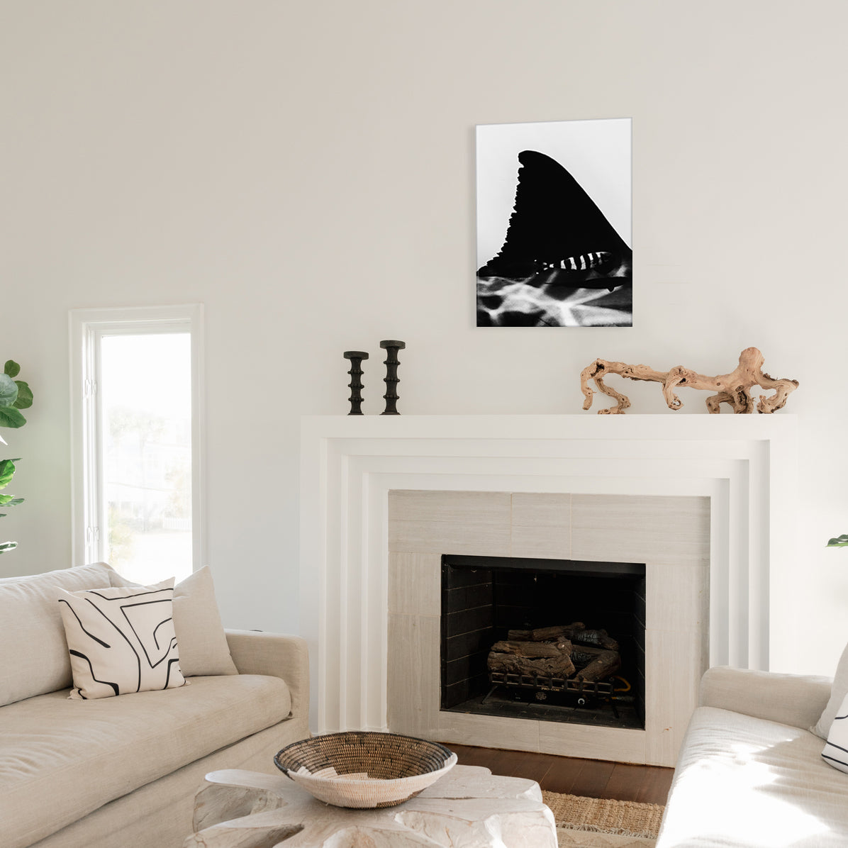 Living room with a fireplace, white walls, and a black and white glass print of a shark fin and striped fish above the mantel.
