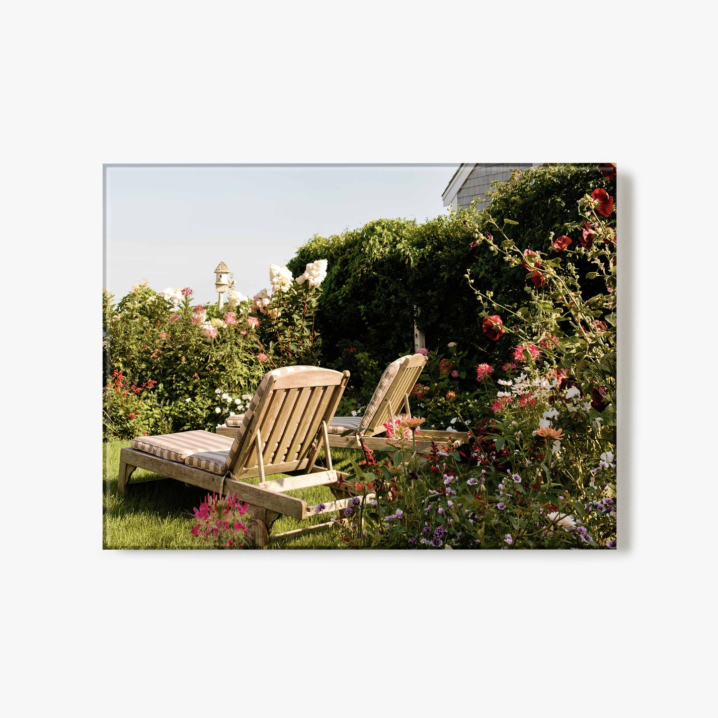Glass print of two wooden chairs in a garden with flowers and greenery