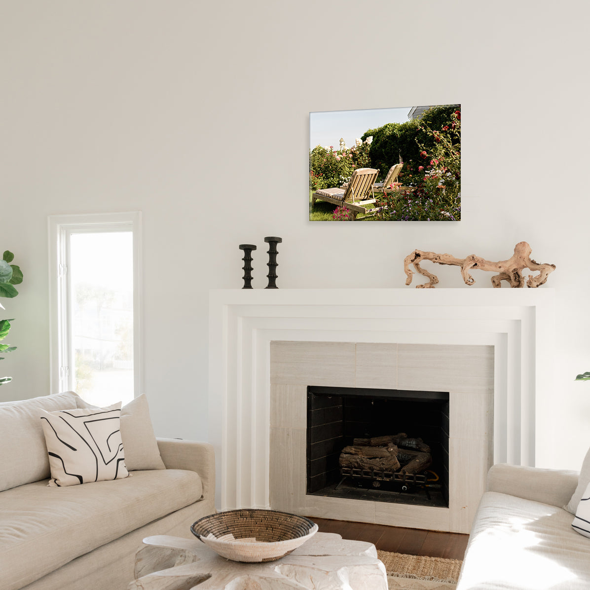 Living room with a fireplace, couch, and a glass print above the mantel featuring two wooden chairs in a lush, floral garden.