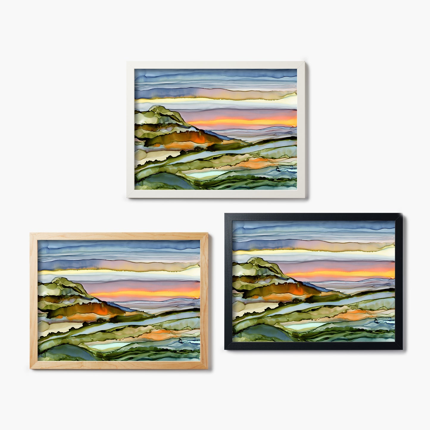 Three framed glass prints of abstract landscape paintings with different color frames on a white background