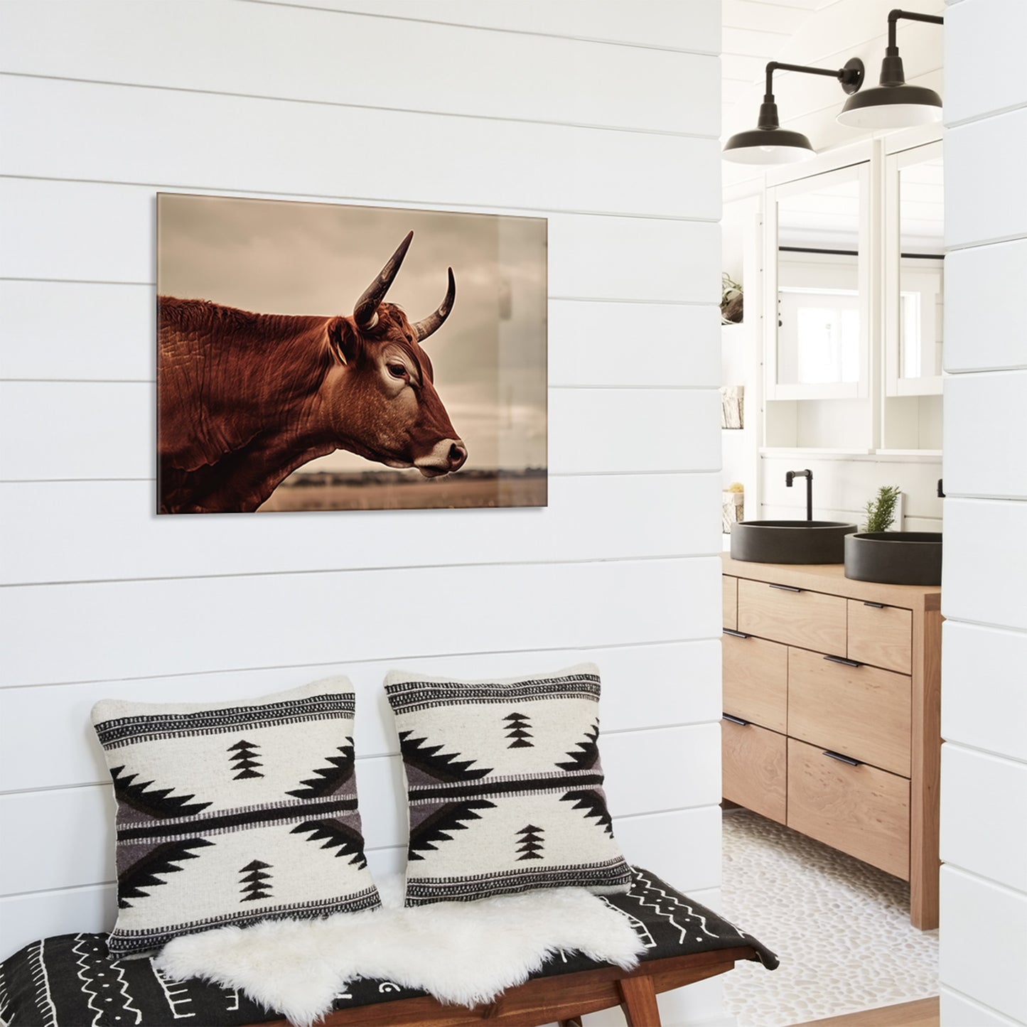 White paneled interior with a glass print of a cow on the wall, patterned pillows on a bench, and wooden cabinets.