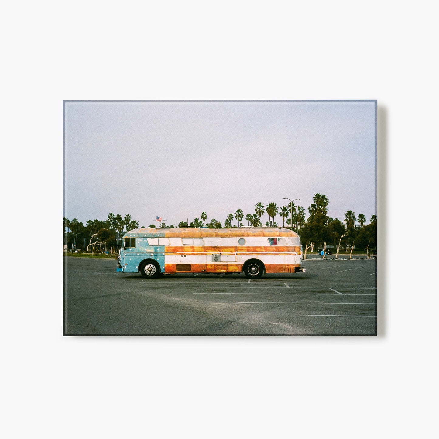 Glass print of a colorful bus in a parking lot with palm trees in the background