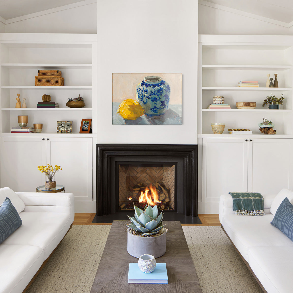 Living room with white walls, a fireplace, and a glass print of a still life painting of a lemon and chinoiserie pot.