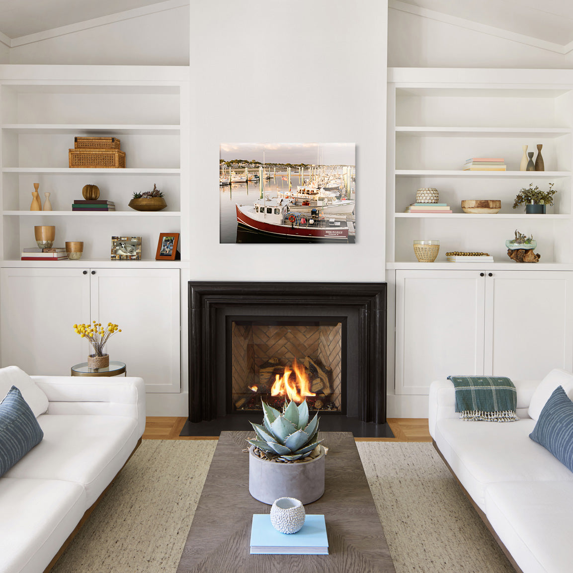 Modern living room with white walls, a fireplace, and a large glass print of a marina of boats above the mantel.