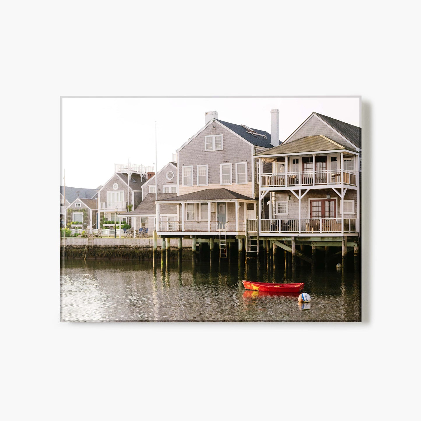 A glass print of a row of houses along a waterfront with a red boat in the foreground.