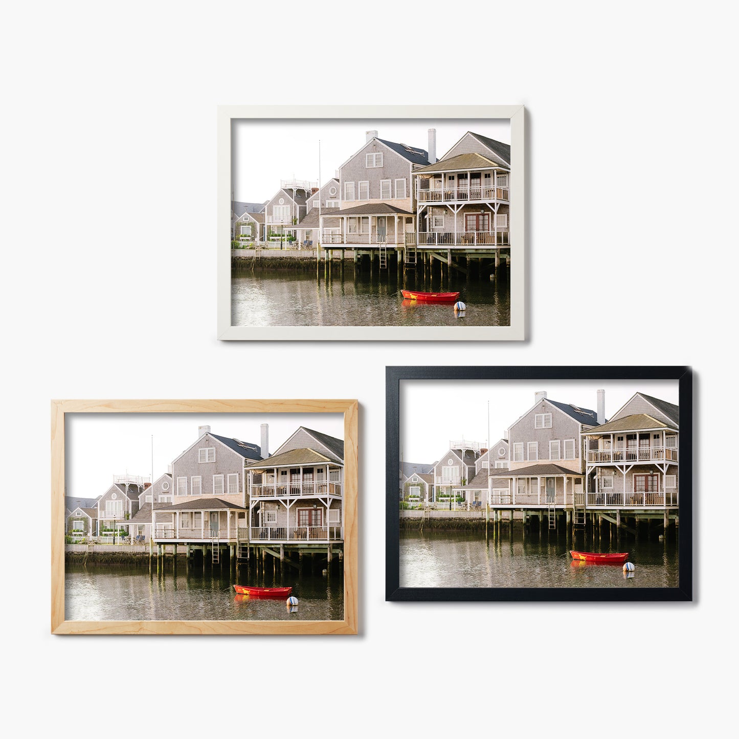 Three framed glass prints of coastal houses with boats on a white background