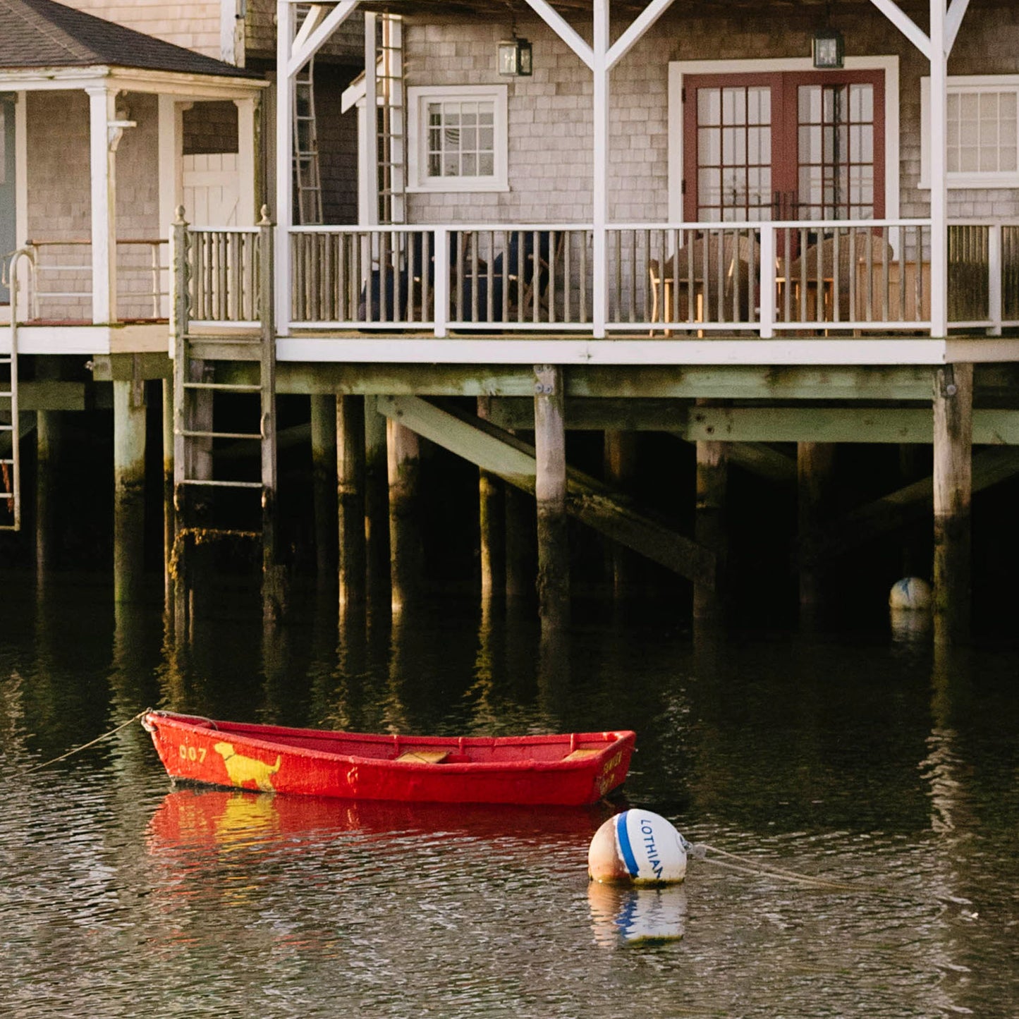 Close up of red rowboat on water near a wooden dock and house