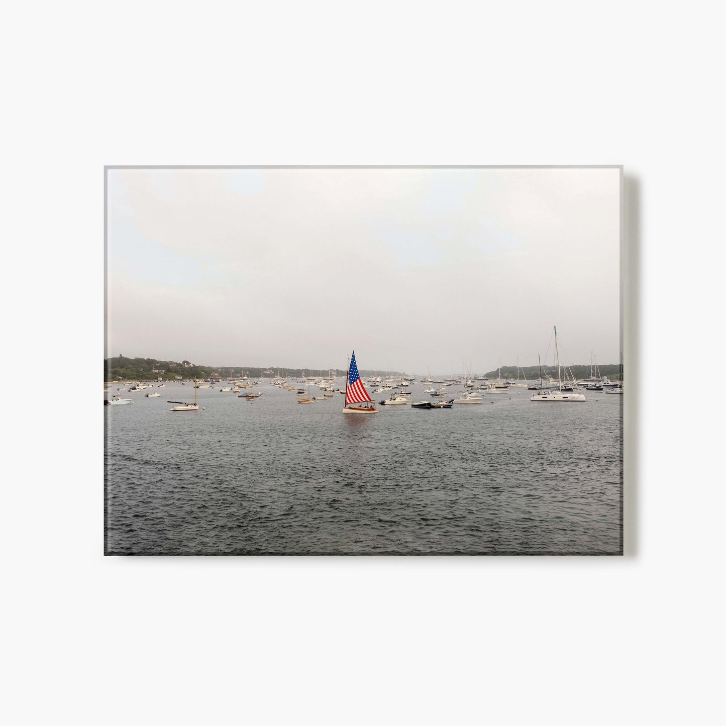 Glass print of a sailboat with an American flag on a body of water with other boats in the background.