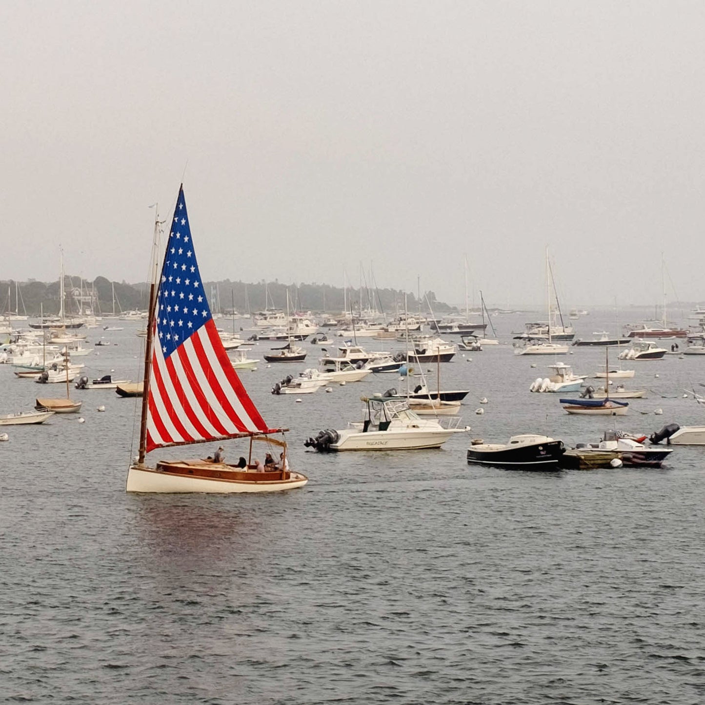 Close up of sailboat with an American flag on a body of water with other boats in the background.