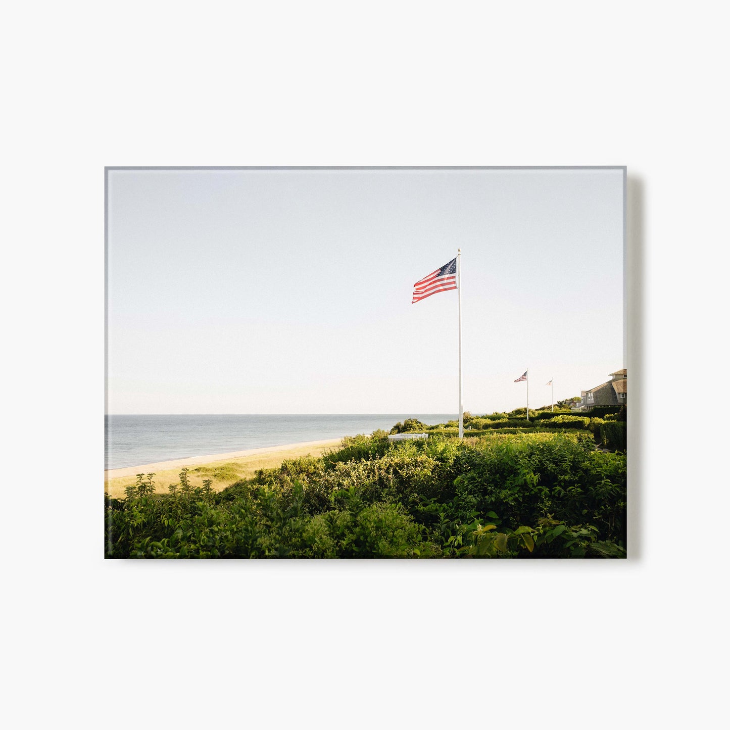 A glass print of American flags on poles with a beach and ocean in the background