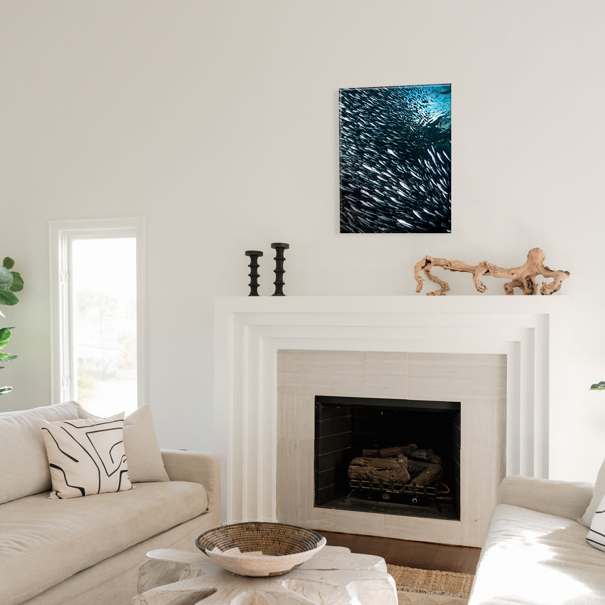 Living room with a fireplace, decorative items, and a large glass print of a school of silver fish on the wall.