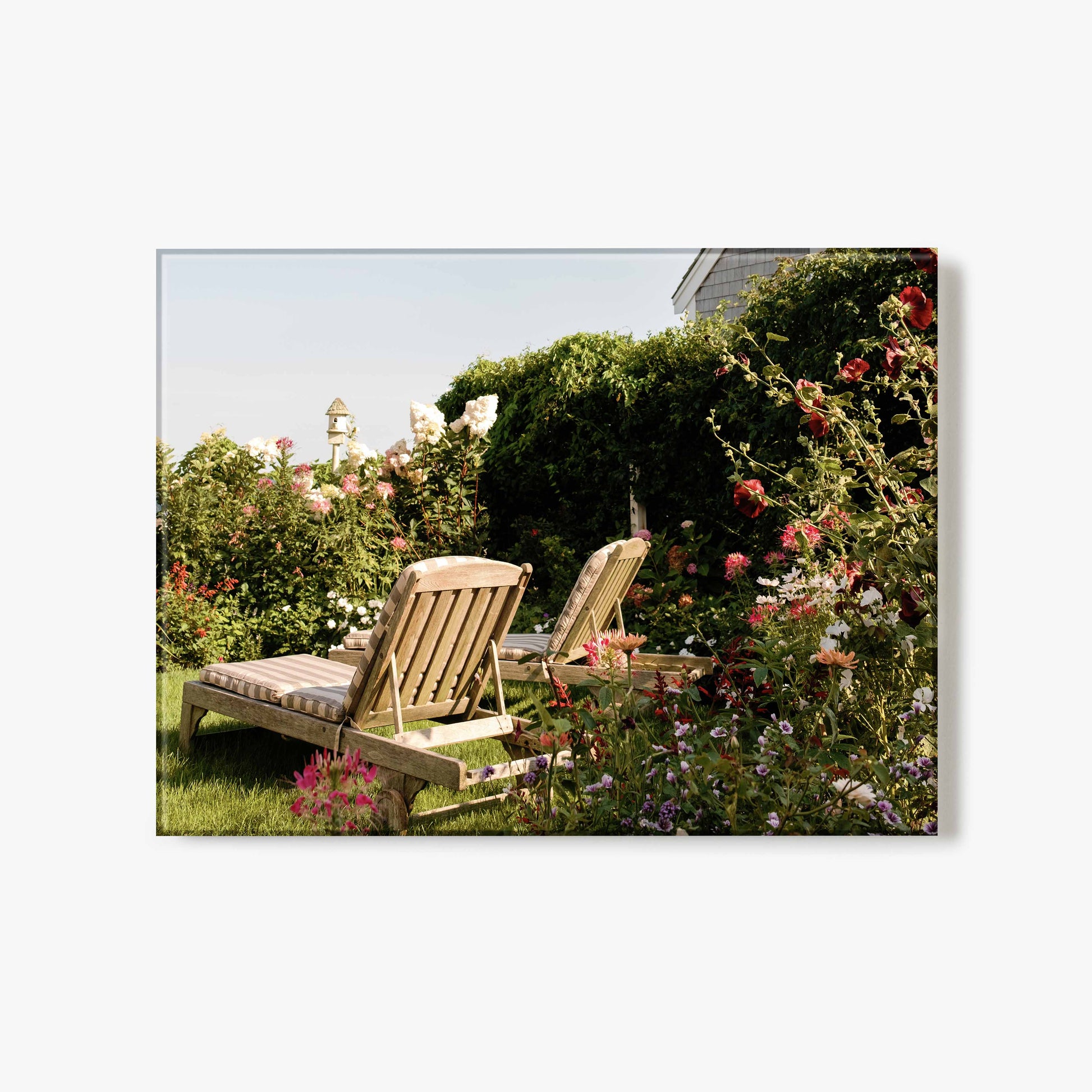 Glass print of two wooden chairs in a garden with flowers and greenery