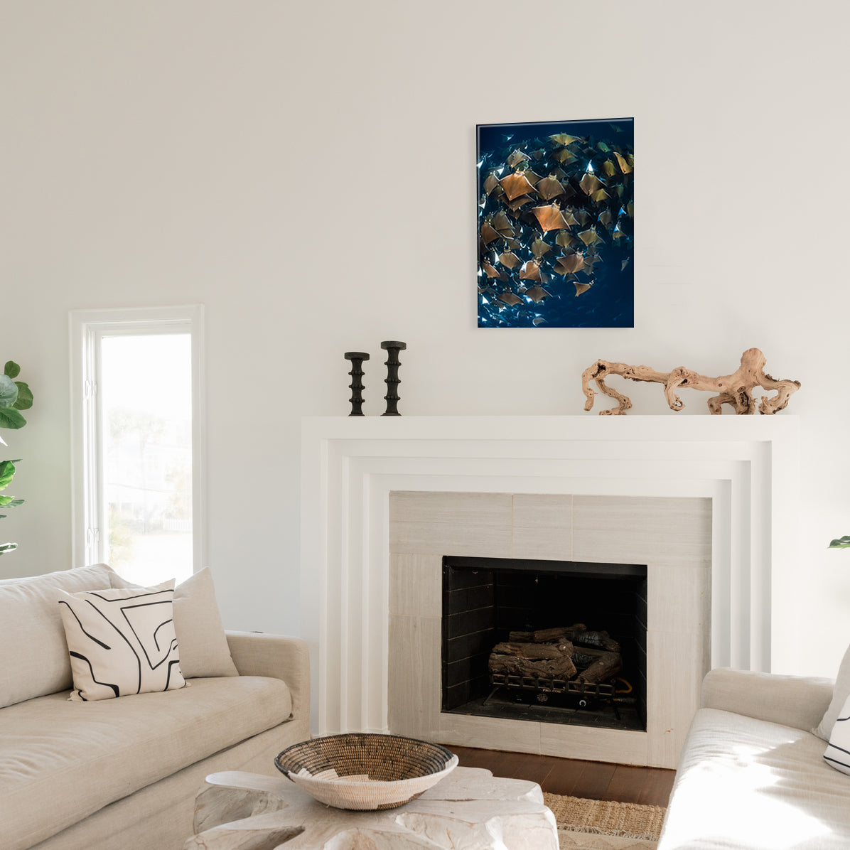Living room with a fireplace, a glass print of swirling devil rays above it, and decorative candlesticks and driftwood.
