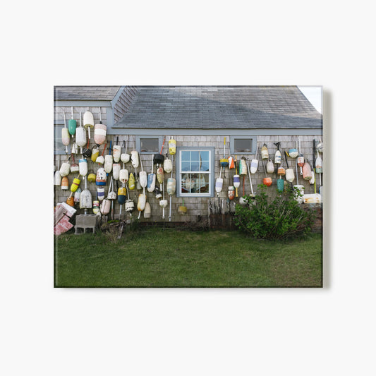 Glass print of a house exterior with a wall of colorful buoys and fishing equipment.