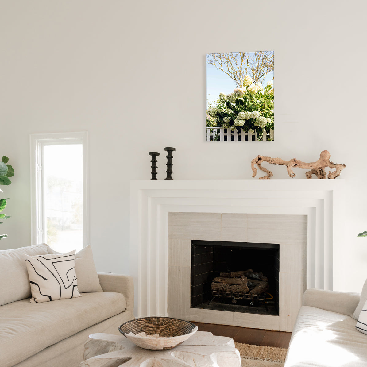 Living room with a fireplace, decorative items, and a glass print on the wall of white hydrangeas over a white picket.