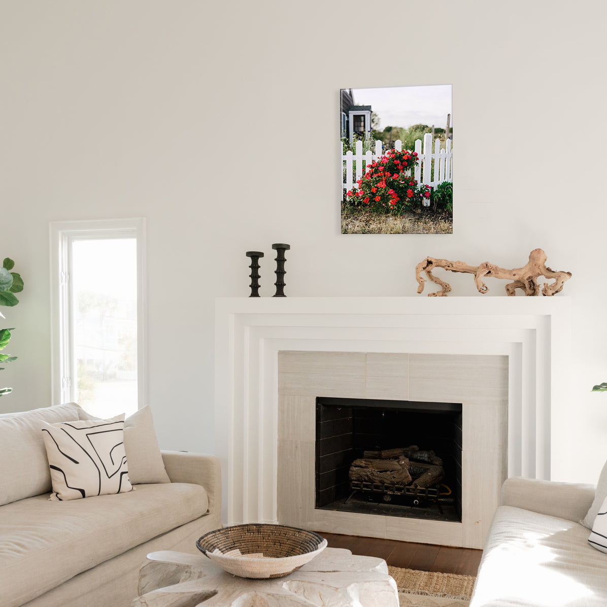Living room with a fireplace, couch, and a glass print of red flowers growing against a white picket fence