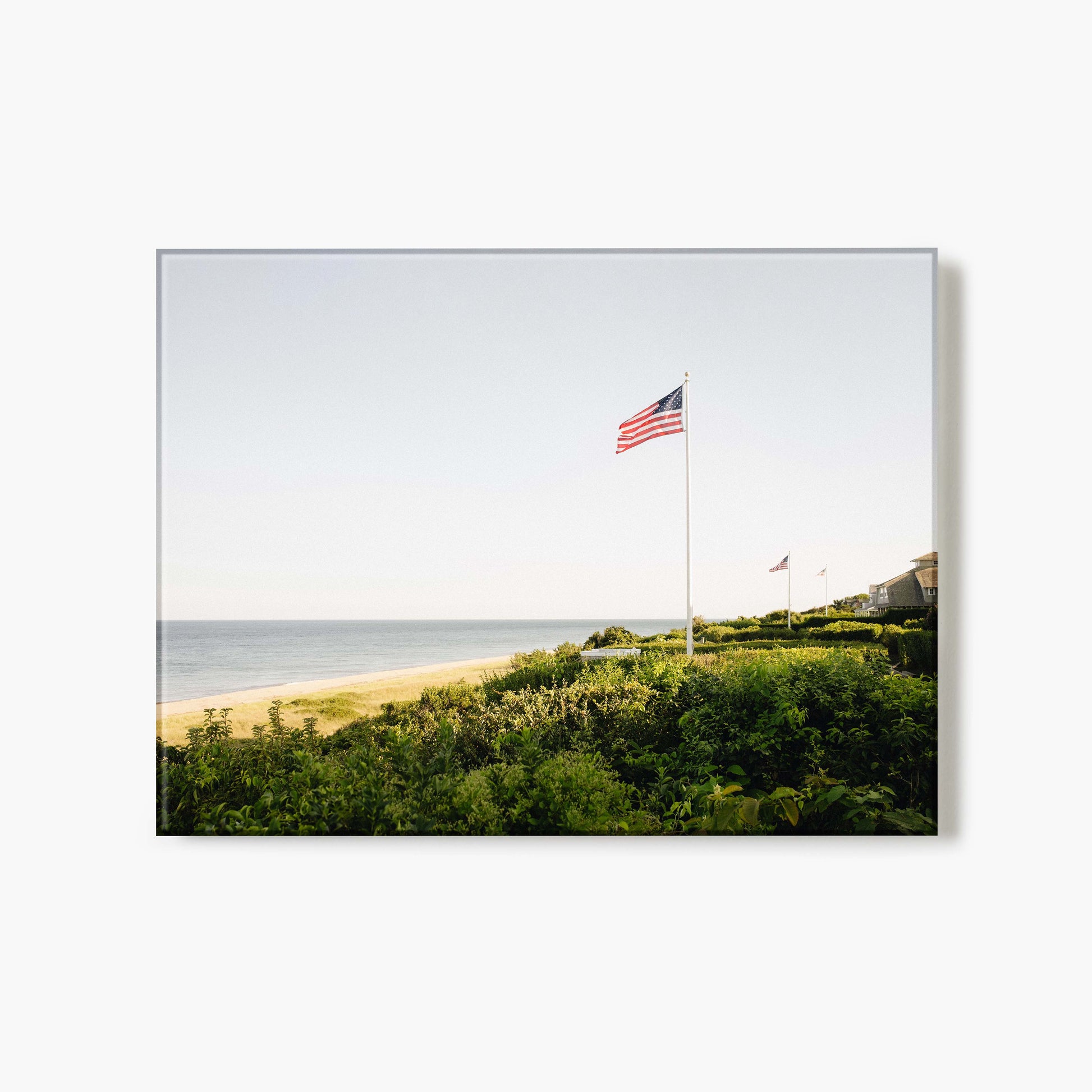A glass print of American flags on poles with a beach and ocean in the background