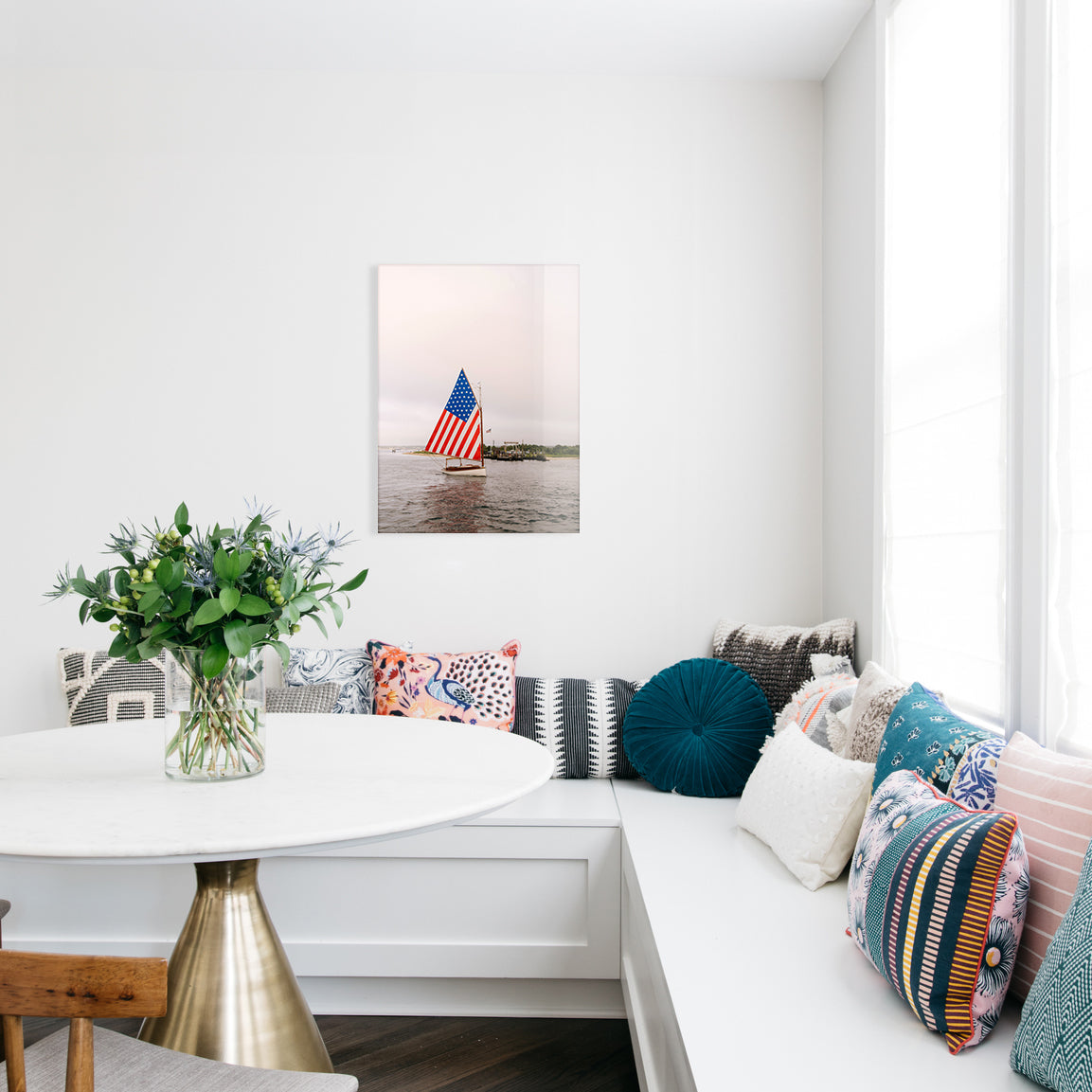 Living room with a white sofa, decorative pillows, a small table with flowers, and a glass print of a sailboat flying a large American flag on the wall.