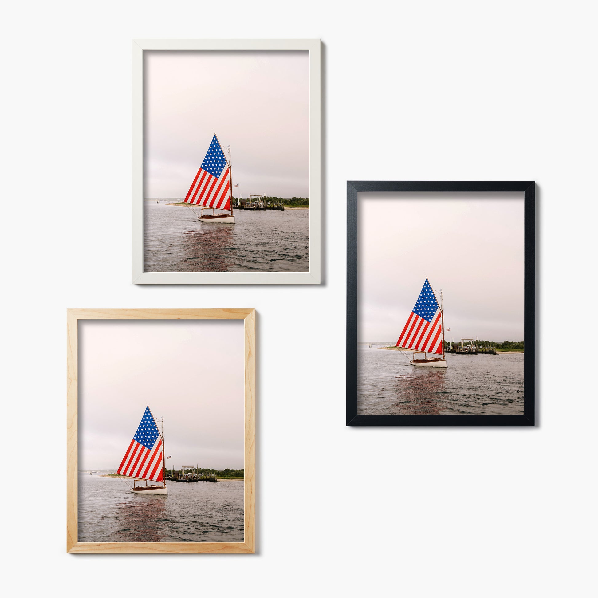 Three framed glass prints of a sailboat with an American flag on a white wall.