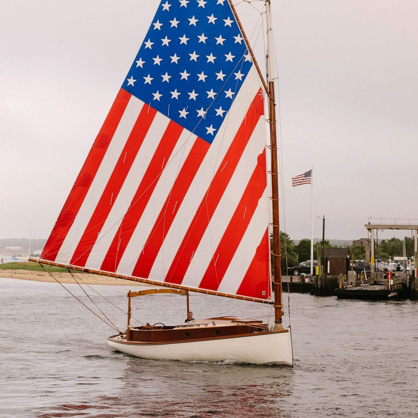 Close up of sailboat with a large American flag on its sail, docked at a harbor.